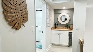 A modern kitchen with white cabinets, a round mirror, and a wooden leaf wall art piece. - Pet-Friendly Paradise with Special Discounts - A Wave from It All Awaits!" (Fort Pierce)