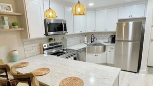 A modern kitchen with white cabinetry, stainless steel appliances, and a central island with woven placemats. - Pet-Friendly Paradise with Special Discounts - A Wave from It All Awaits!" (Fort Pierce)