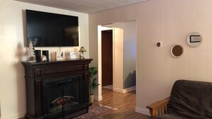 Una sala de estar con chimenea, televisor montado en la pared, sofá y un pasillo que conduce a otra habitación.