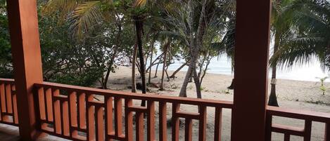A wooden deck with a view of a beach and palm trees.