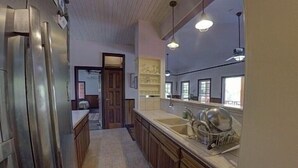 Una cocina con armarios de madera, un refrigerador de acero inoxidable, un lavaplatos y lámparas colgantes.