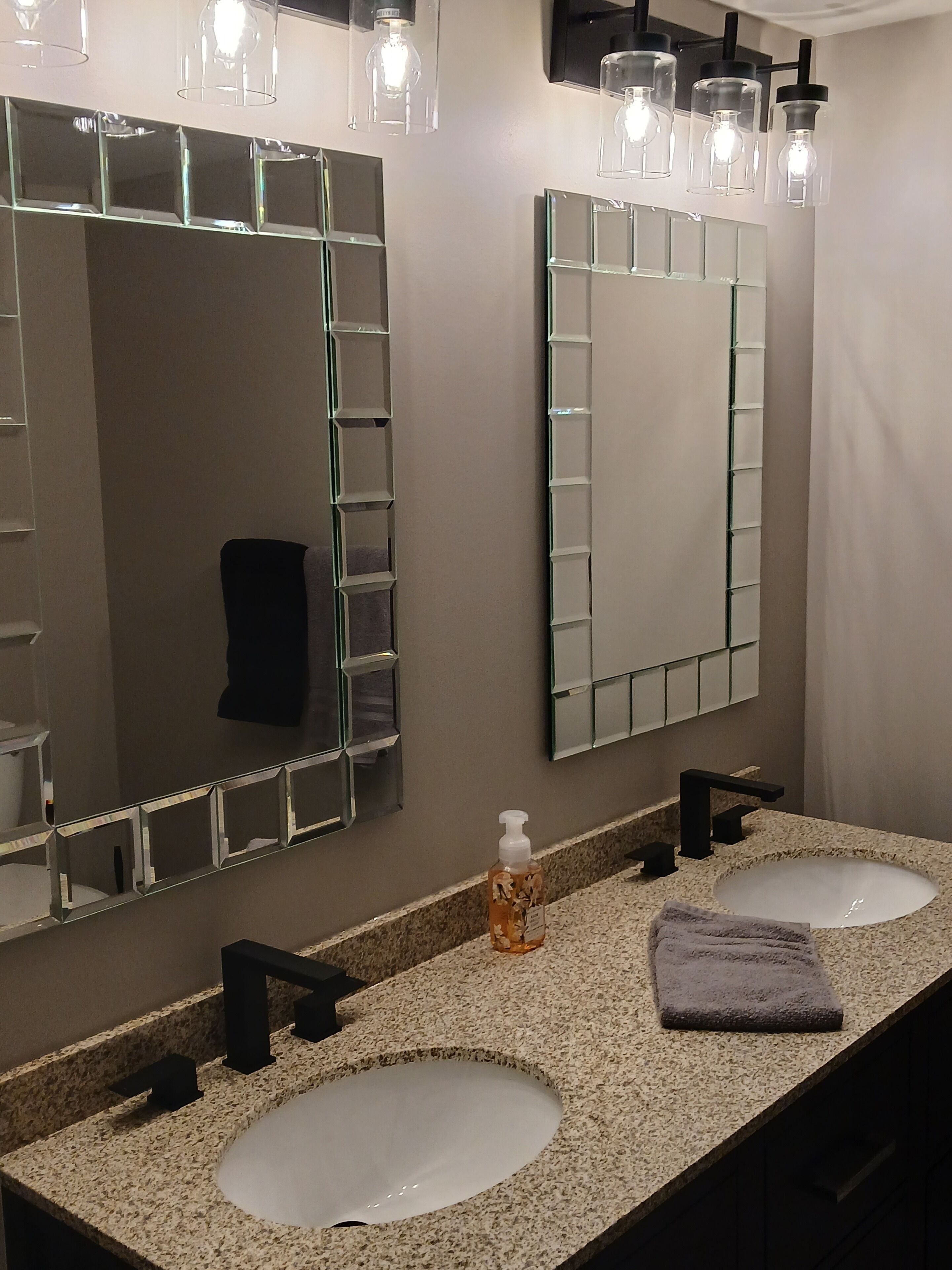 A bathroom with two sinks, a large mirror, and a bottle of hand soap.