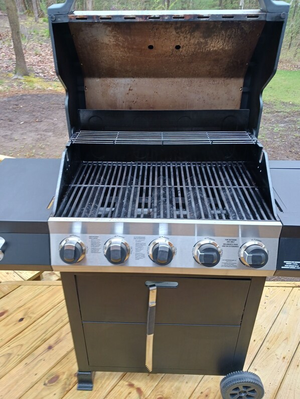 Ein tragbarer Grill mit vier Reglern, einem Deckel und einem Seitenbrenner.