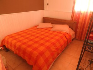 Ein kleines Zimmer mit einem Einzelbett, einem Holzkopfteil, einer orangefarbenen Bettdecke mit Karomuster und weißen Kissen.