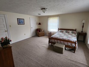 Ein Schlafzimmer mit einem Bett, einem Sessel, einer Lampe, einem Fenster mit Vorhängen und einer Tür.