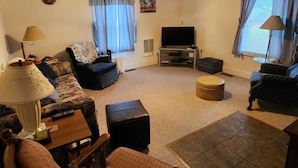A cozy living room with a TV, comfortable seating, a ceiling fan, and a fireplace.