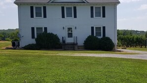 A two-story white house with a front porch, a satellite dish, and a small shed to the left.