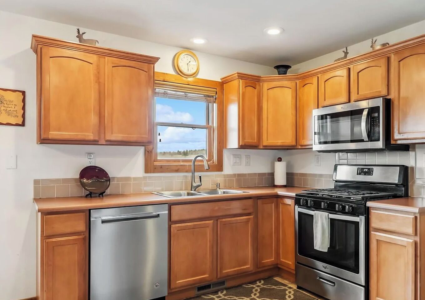 A kitchen with wooden cabinets, stainless steel appliances, a window, and a clock.