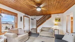 Un salon chaleureux avec un plafond en bois, un escalier et une grande fenêtre donnant sur un paysage enneigé.