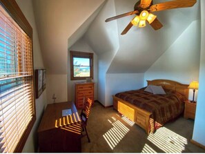 Cozy loft-style room with a wooden bed, desk, and ceiling fan.