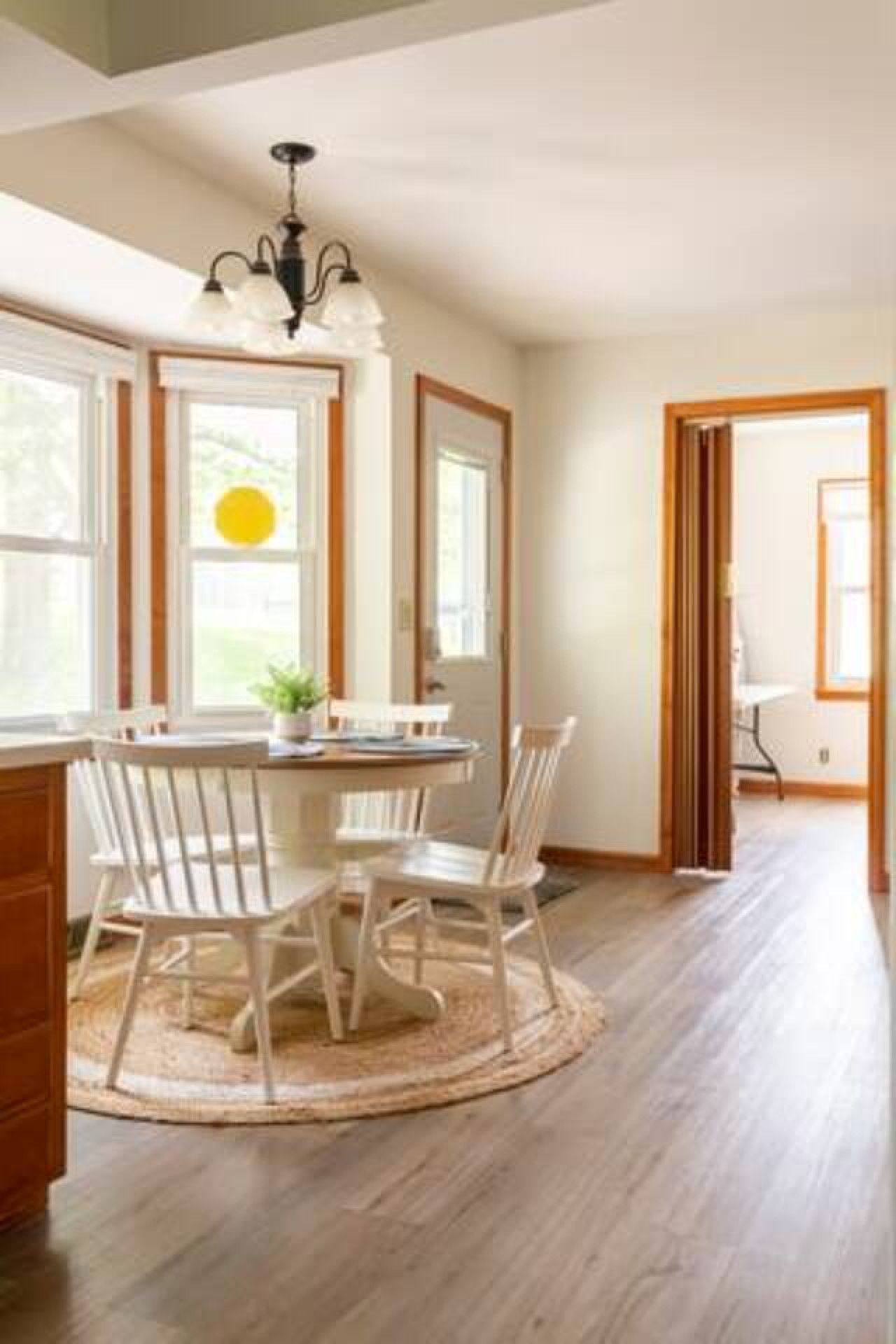 A dining area with a round table and chairs, a chandelier, and a view of the outdoors through large windows.