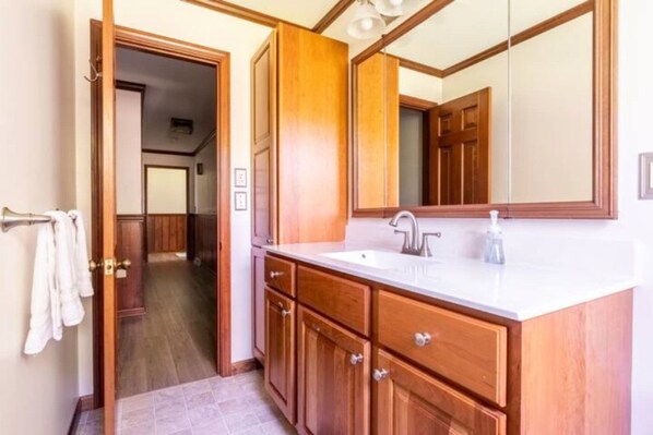 Un baño con armarios de madera, un lavabo blanco y un espejo grande.