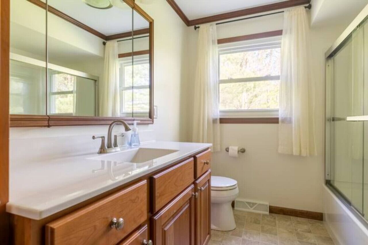 Un baño con lavamanos blanco, tocador de madera, un espejo grande, inodoro y zona de ducha.