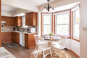 A kitchen with wooden cabinets, a white countertop, and a dining area with a round table and white chairs. - 85 acre private estate (Logan)