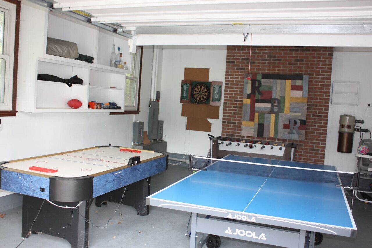A room with a foosball table, a ping pong table, and a dartboard.