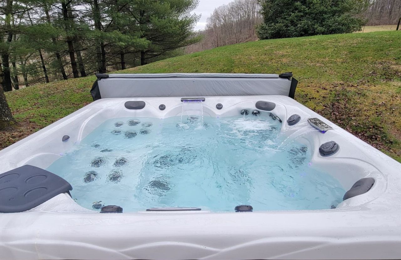 An outdoor hot tub with a cover, surrounded by a grassy area and trees.