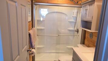 Une petite salle de bain comprenant une douche, des toilettes et un lavabo, avec un plafond et des murs en bois.