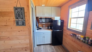 Cocina compacta con paredes de madera, un refrigerador negro, un microondas y una ventana con vistas.