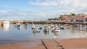 Un port où sont amarrés des bateaux, une plage de sable et des bâtiments en arrière-plan.