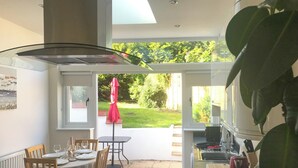 Une cuisine moderne avec un coin repas vitré, un parasol rouge et une vue sur un jardin.