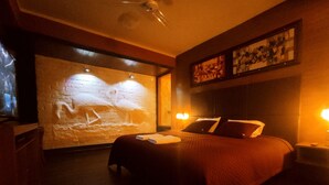 A dimly lit room with a bed, a wall with a light sculpture, and a ceiling fan. - Hostal Cagnapa Restobar (Uyuni)