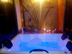 A hot tub with a wooden bench, candles, and a plant in the background. - Hostal Cagnapa Restobar (Uyuni)