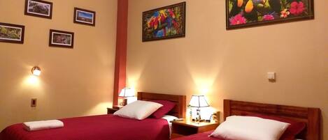 Una habitación de hotel con dos camas, cada una con ropa de cama roja y almohadas blancas, y un cuadro de loros en la pared.
