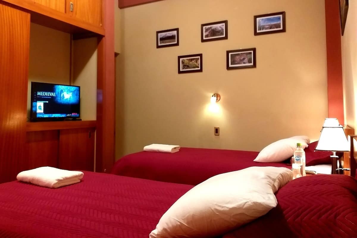 Habitación de hotel con dos camas, un televisor a la izquierda y una pared con cuatro cuadros enmarcados.