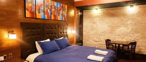 Ein Hotelzimmer mit einem großen Bett, einem Kopfteil, einem Wandbild, einem Deckenventilator und einer Ziegelwand mit geschnitztem Dekor.