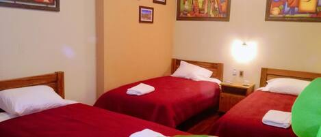 A hotel room with two beds, each with a red bedspread and white pillows, and a large green plant in the foreground.