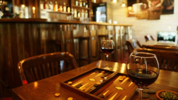 A bar area with wooden furniture, a bottle rack, and a wine glass on the table. - Hostal Cagnapa Restobar (Uyuni)