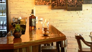 A bar area with a wooden counter, a bottle of Jack Daniel's whiskey, a candle, and a coffee-themed wall art. - Hostal Cagnapa Restobar (Uyuni)
