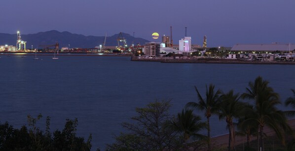 A coastal industrial area with cranes, buildings, and a sunset over the water.