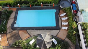 Vista aérea de una piscina con sillas de descanso y una zona de estar cubierta.
