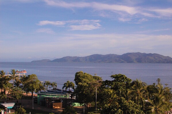 A coastal view with mountains in the distance, a beach with palm trees, and a building with a green roof. - Beautiful Beachfront location. (North Ward)