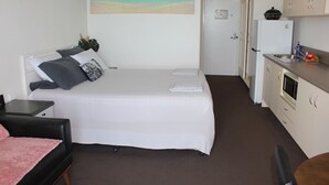 Un dormitorio con cama, mesita de noche y velador. Hay un cuadro con una escena de playa en la pared.