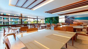 A modern restaurant with wooden furniture, large windows, and a view of the ocean.