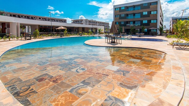 A swimming pool with a unique tile design, surrounded by outdoor seating and a modern building in the background.