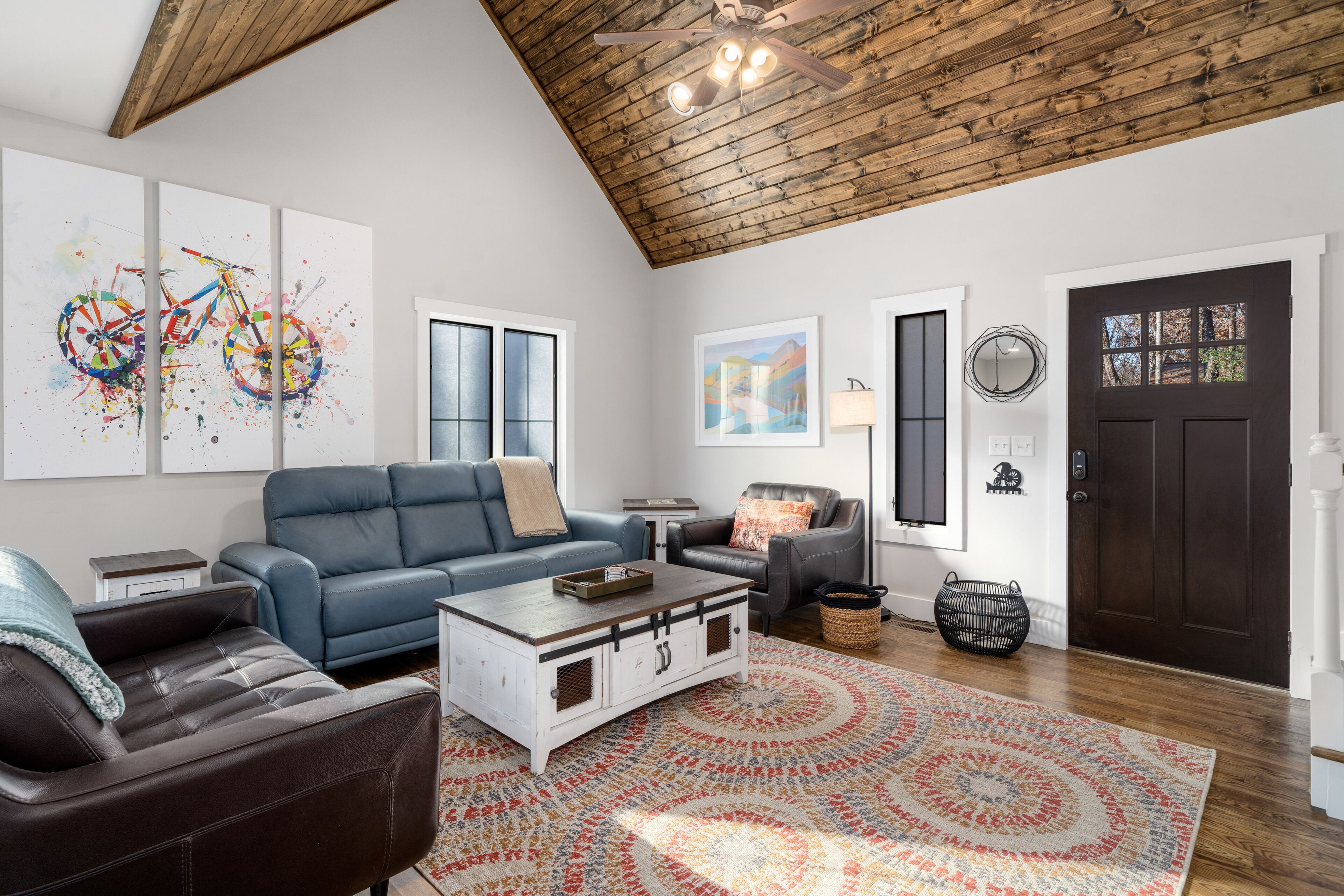A spacious living room with a high wooden ceiling, a blue sofa, a white coffee table, and a patterned rug.