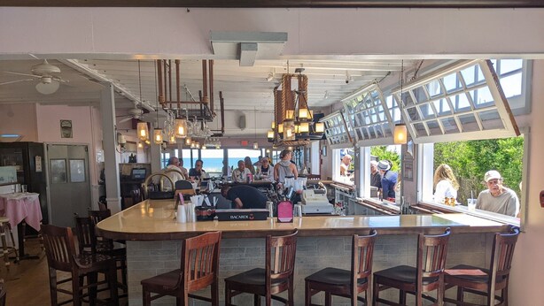 A bar area with wooden chairs, a bar counter, and hanging lights. - Paradise on the Great South Bay (Cherry Grove)