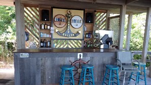 A wooden deck with a bar area featuring a nautical theme, including a ship's wheel and shelves with bottles. - Paradise on the Great South Bay (Cherry Grove)