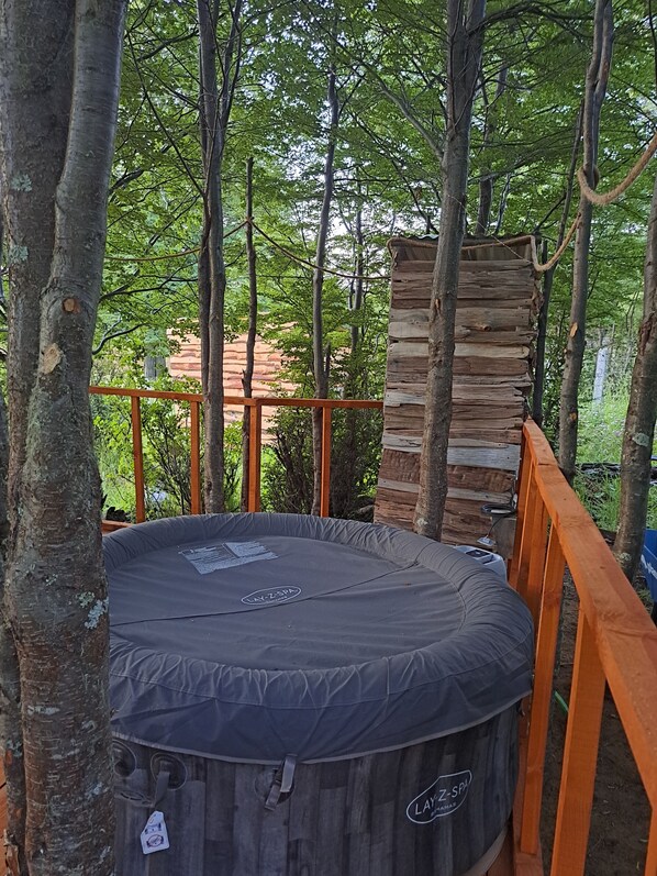 Un jacuzzi rodeado de árboles, con una estructura de madera cerca y una barandilla de metal.