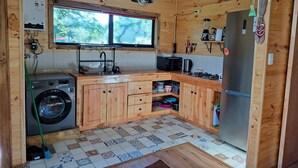 Une cuisine de taille réduite, dotée de meubles en bois, d’un lave-linge, d’un four à micro-ondes et d’un réfrigérateur.