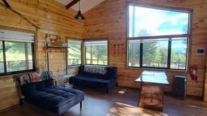 Une pièce spacieuse aux murs en bois et au plafond en pente, comprenant un canapé, une petite table et de grandes fenêtres donnant sur l’extérieur.