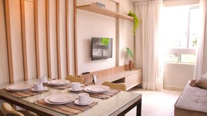 A dining area with a glass table set for four, surrounded by chairs. A television is mounted on the wall above the table. - Apart na Orla de Cabo Branco - Carpediem (João Pessoa)