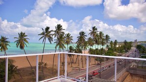 A balcony with a view of a beach, palm trees, and a road with vehicles. - Apart na Orla de Cabo Branco - Carpediem (João Pessoa)