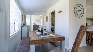 Un comedor con una mesa de madera dispuesta para dos personas, una silla de mimbre y un reloj de pared.