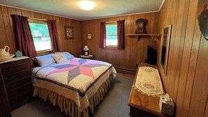 Quarto com cama, cômoda, mesa de cabeceira e uma pequena mesa com abajur.