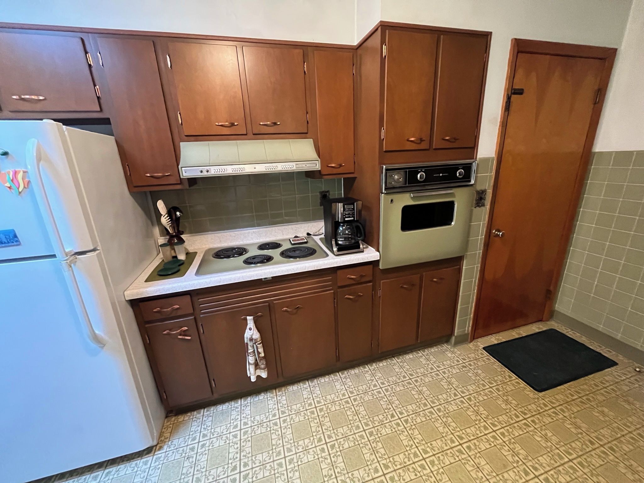 A compact kitchen with wooden cabinets, a white refrigerator, a stove, and an oven.