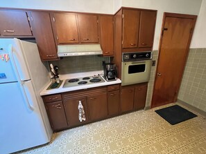 A compact kitchen with wooden cabinets, a white refrigerator, a stove, and an oven.